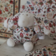 Le XCOMM_DOUDOU ÂNE FANTAISIE INDIENNE, une peluche au corps rond orné d’un motif floral, dotée de grandes oreilles et dont le visage, les pattes et les pieds sont en tissu blanc, est posée sur une surface en tissu à motifs, avec des motifs décoratifs similaires en arrière-plan. la marque Toile de Jouy
