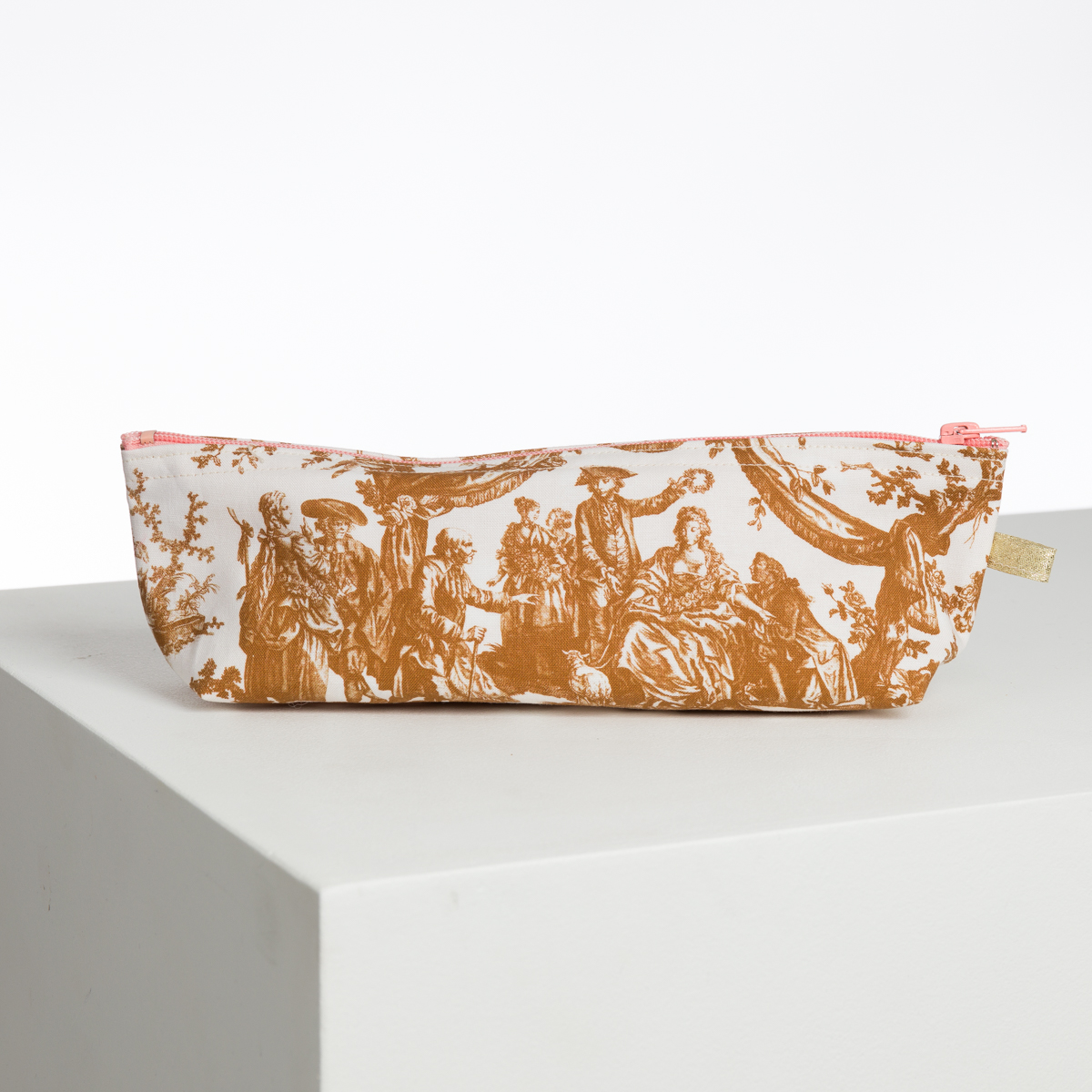 Le XCOMM_BIC BALLON PESTO est un étui à crayons rectangulaire avec une fermeture éclair rose, présentant une scène pastorale vintage brune sur fond blanc et exposée sur une surface blanche minimaliste. la marque Toile de Jouy