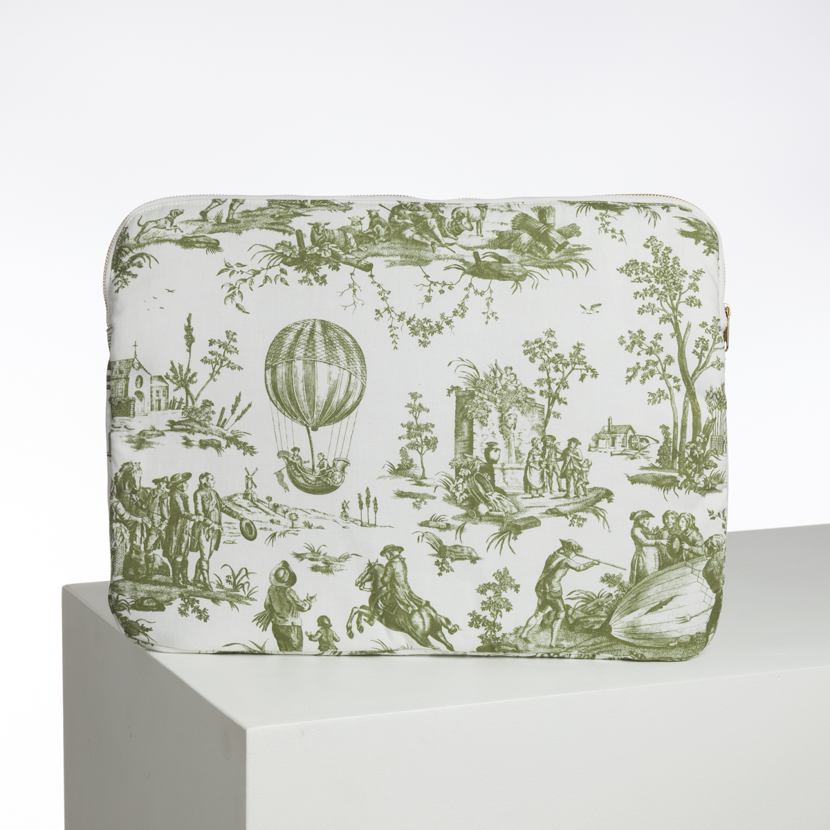 La pochette XCOMM_BIC BALLON PESTO présente un motif de toile pastorale verte et blanche avec des personnages, des arbres, une maison et une montgolfière, représentés debout sur une plate-forme géométrique blanche. la marque Toile de Jouy