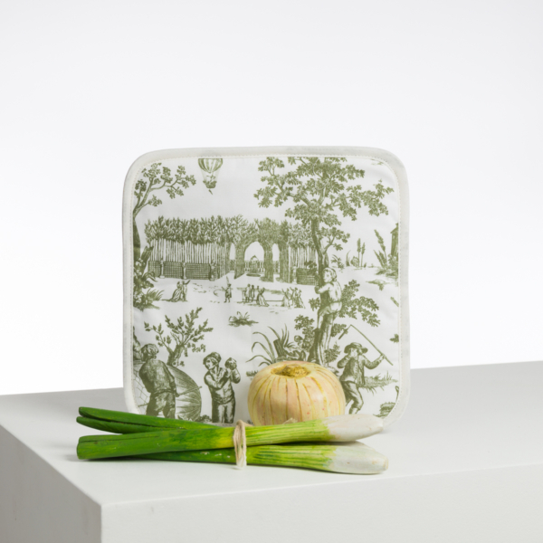 Le cache-pot XCOMM_BIC BALLON PESTO, représentant une scène pastorale verte, est présenté derrière un oignon jaune et des oignons verts frais sur une surface blanche, sur un fond blanc uni. la marque Toile de Jouy