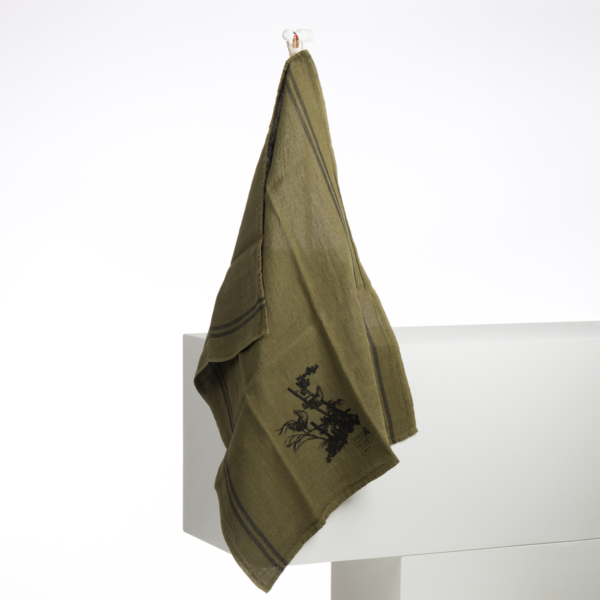 Le torchon XCOMM_GRAND TORCHON BRODE ROSIERE CUMIN, un torchon vert avec une broderie florale noire et deux bandes sombres, est suspendu à un crochet sur une surface blanche. la marque Toile de Jouy