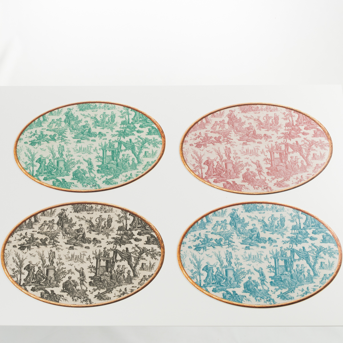 Quatre sets de table XCOMM_SET DE TABLE OVAL OFFRANDE A L'AMOUR ovales sur une surface blanche, chacun avec une scène pastorale vintage en vert, rose, noir et bleu, et des bordures dorées sur le pourtour. la marque Toile de Jouy
