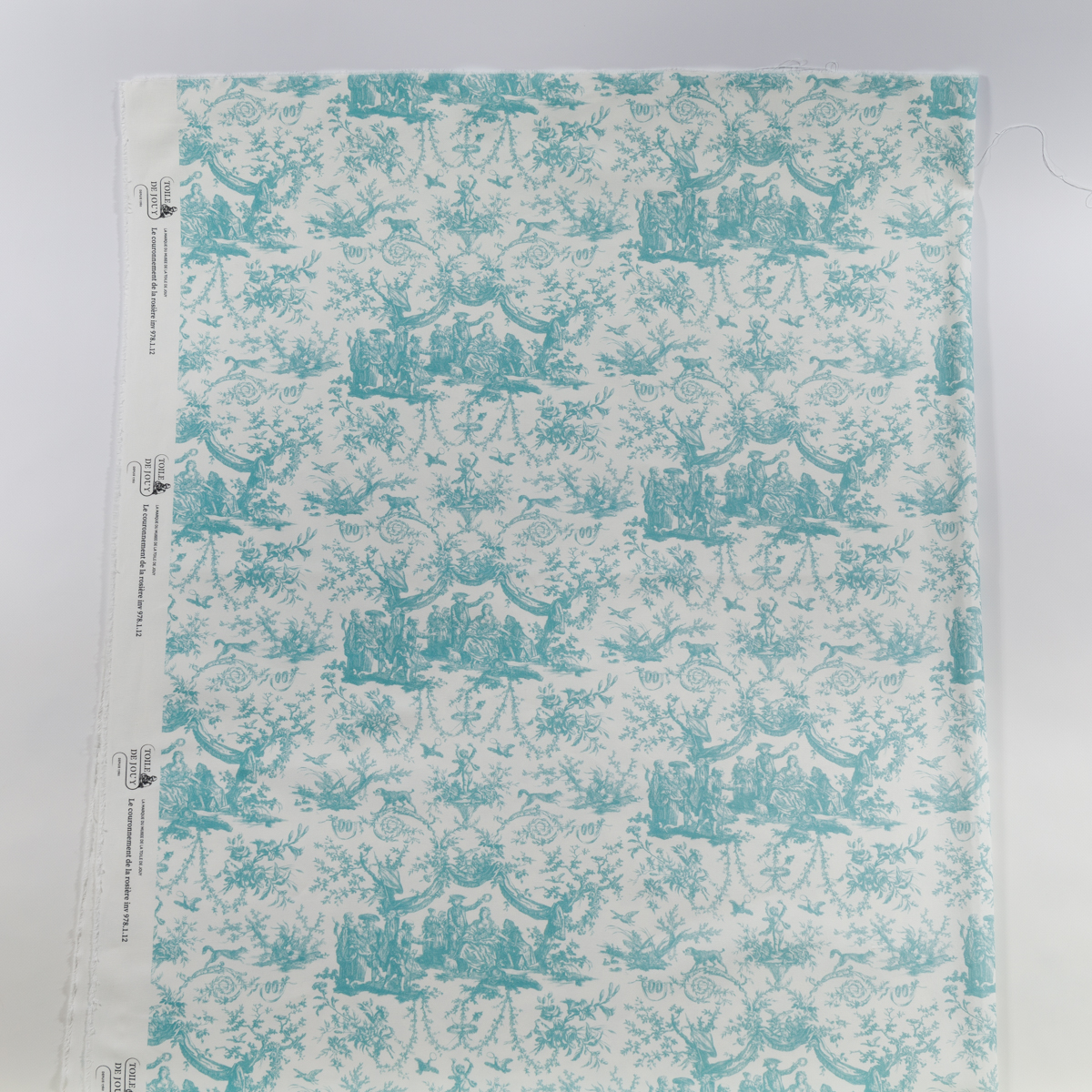 TISSU "LES 4 PARTIES DU MONDE" VERT JUNGLE : Un tissu vert sur le thème de la jungle avec un motif répétitif de scènes pastorales, de fleurs ornées et de rinceaux, présenté à plat avec une lisière le long du bord gauche. la marque Toile de Jouy