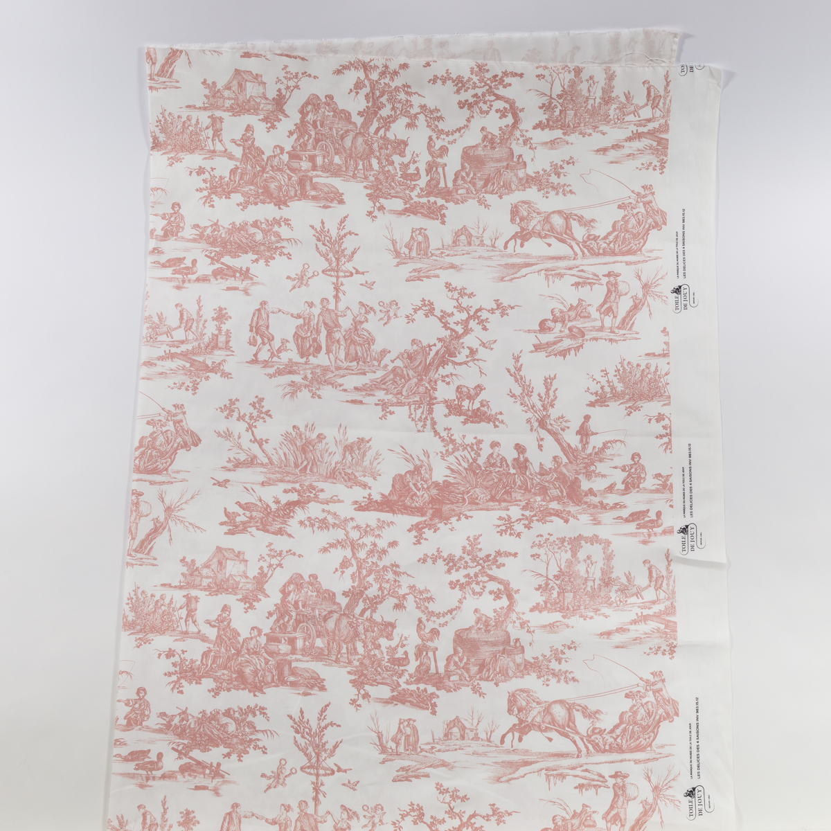 Un morceau de tissu "TISSU 'LES 4 PARTIES DU MONDE' VERT JUNGLE", présentant des scènes pastorales complexes en vert jungle avec des personnes, des arbres et des animaux dans des motifs répétitifs. Les bords ne sont pas finis avec des marques de fabricant sur le côté droit. la marque Toile de Jouy