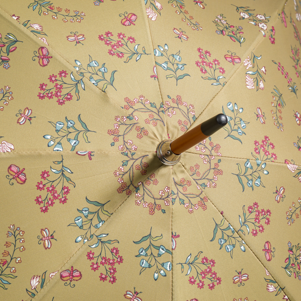 Voici une phrase réécrite à partir des informations fournies sur le produit : Gros plan sur un parapluie ETIQUETTE DE VOYAGE « FANTAISIE INDIENNE » ouvert, doté d’un manche en bois, mettant en valeur un tissu jaune orné d’un motif fantaisiste de fleurs et d’abeilles roses, blanches et vertes. la marque Toile de Jouy