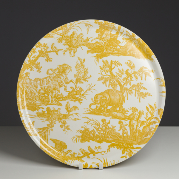 L'assiette ronde XCOMM_PLATEAU ROND 46CM DELICES BLEU présente une scène pastorale bleue complexe avec des personnes, des animaux et des arbres sur un fond blanc, présentée à la verticale sur un fond sombre. la marque Toile de Jouy