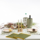 Une table à manger avec le XCOMM_SET DE TABLE/2 COURONNEMENT CUMIN, comprenant deux couverts, des serviettes vertes, des feuilles et des plantes d'automne, des bougeoirs en bois, des verres à vin, un cache-bouteille vert et de l'herbe décorative. la marque Toile de Jouy