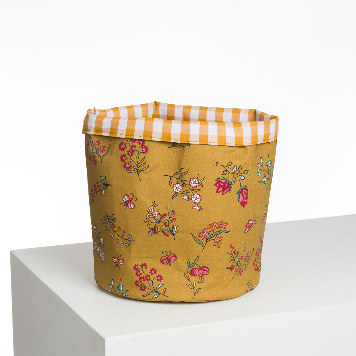 Le XCOMM_CAPE DE PLUIE SEMIS DE FLEURS est un panier de rangement en tissu avec une base florale jaune et un bord à carreaux jaunes et blancs, présenté sur une surface blanche sur un fond blanc uni. la marque Toile de Jouy