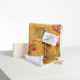 Une pile de tampons en coton réutilisables XCOMM_CAPE DE PLUIE SEMIS DE FLEURS jaunes à motifs floraux, attachés avec de la ficelle, se trouve à côté d'un savon blanc "Savon de Marseille" sur une surface blanche ; un tampon est déplié devant. la marque Toile de Jouy