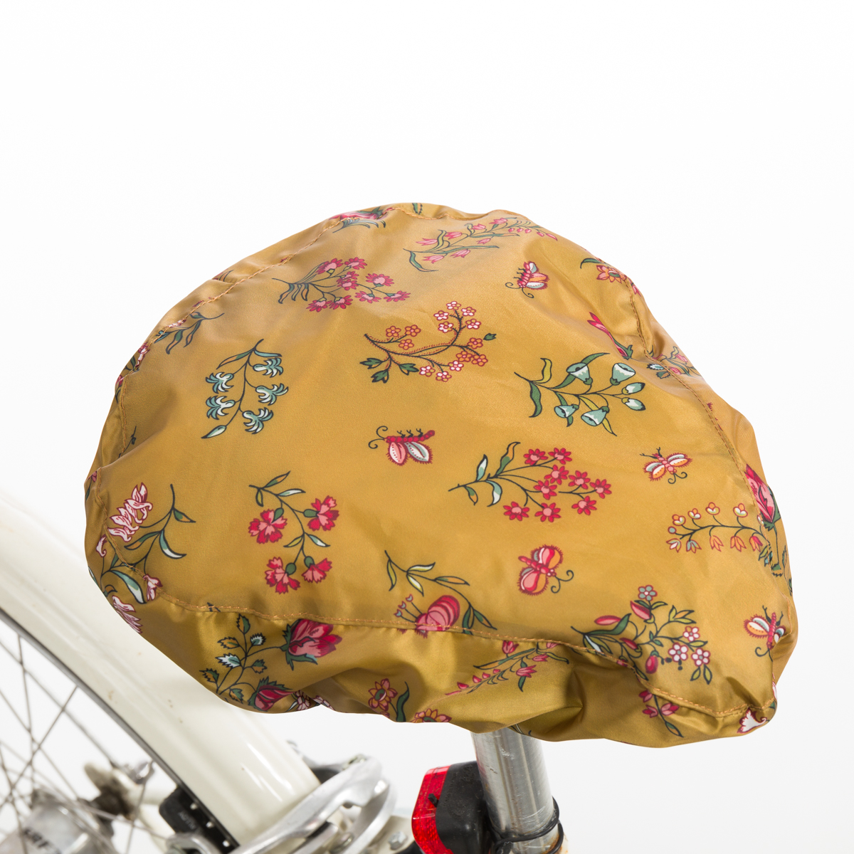 La XCOMM_CAPE DE PLUIE SEMIS DE FLEURS est une housse de selle de vélo jaune avec un motif floral coloré de fleurs roses, bleues et vertes, montrée installée sur une selle de vélo avec une partie du cadre blanc visible. la marque Toile de Jouy