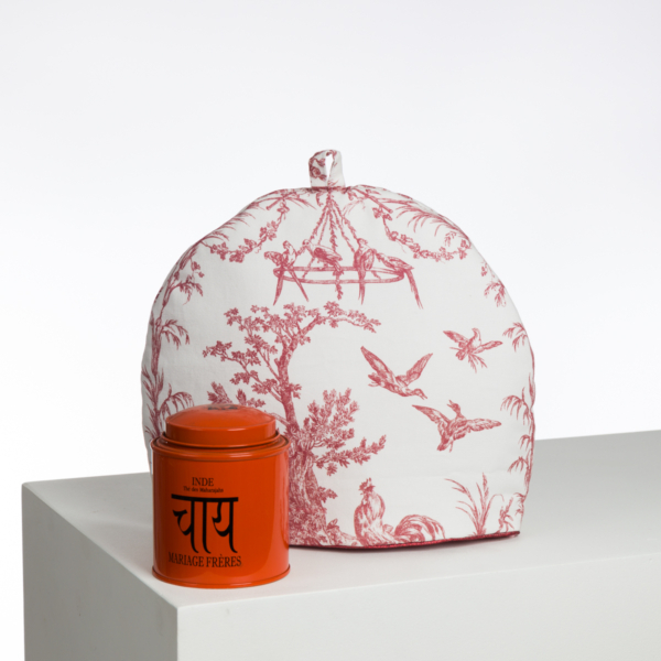 Le sac XCOMM_LUNCH BAG ESCARPOLETTE ROUGE, doté d'un motif blanc et rouge et d'une poignée supérieure, est présenté à côté d'une boîte "Inde" orange avec des caractères hindis, tous deux placés sur une surface blanche sur un fond uni. la marque Toile de Jouy