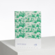 Le carnet XCOMM_EVERYDAY LISTS COURONNEMENT VERT PRAIRIE présente une couverture blanche avec des illustrations tropicales vertes et des palmiers, se tient debout sur une surface blanche et comporte une bande blanche en bas avec du texte et un petit logo. la marque Toile de Jouy