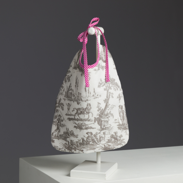 Le XCOMM_LUNCH BAG ESCARPOLETTE ROUGE est un sac à main blanc avec des scènes pastorales noires et des poignées rayées rose vif et blanc nouées par un nœud, présenté sur un support blanc sur un fond gris foncé. la marque Toile de Jouy