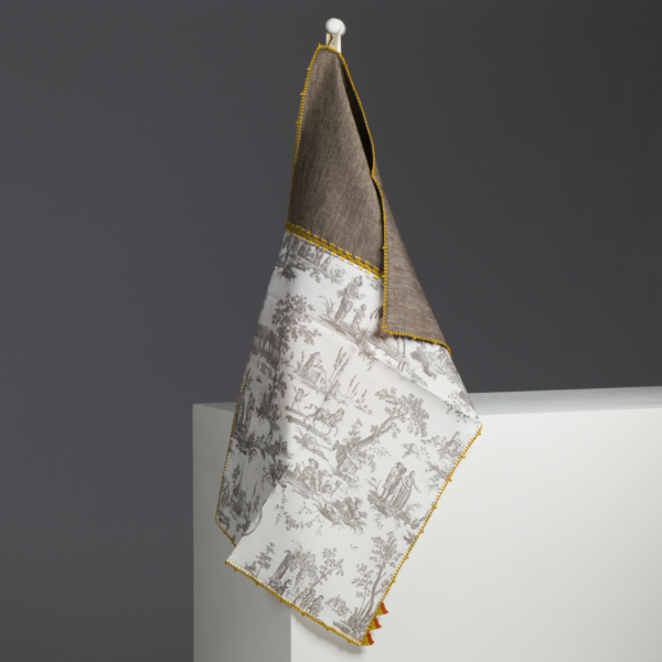 Le sac XCOMM_LUNCH BAG ESCARPOLETTE ROUGE présente un design bicolore avec un dessus marron, un dessous blanc et un motif de toile pastorale grise, présenté sur un crochet blanc sur un fond minimaliste gris et blanc. la marque Toile de Jouy