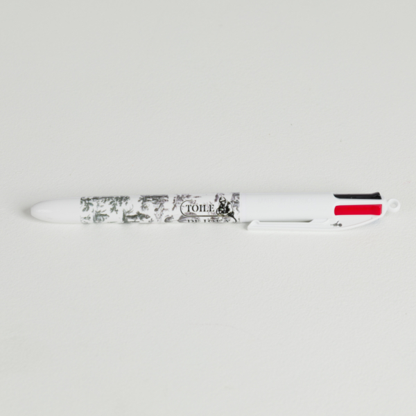 Un stylo à bille multicolore blanc avec des motifs noirs et blancs et "XCOMM_LUNCH BAG ESCARPOLETTE ROUGE" sur le corps, posé sur une surface blanche. Le stylo est doté de languettes de sélection d'encre rouge, noire et bleue. la marque Toile de Jouy