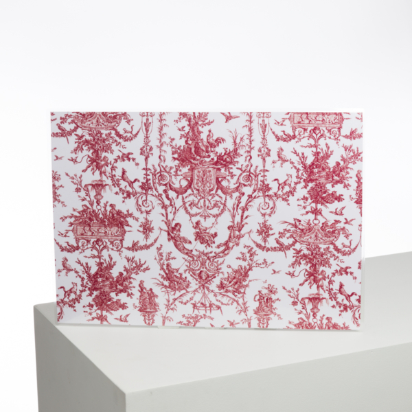 Le XCOMM_LUNCH BAG ESCARPOLETTE ROUGE est présenté à la verticale sur un piédestal géométrique blanc, mettant en valeur son motif de toile rouge et blanche orné de motifs et de figures classiques complexes sur un fond uni. la marque Toile de Jouy