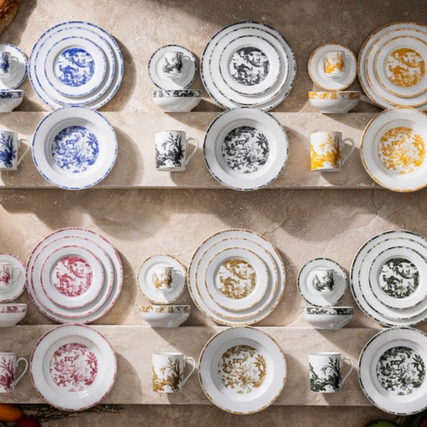 Vue de dessus de douze ensembles VAISSELLE PILLIVUYT - plats, tasses et soucoupes en porcelaine à motifs bleus, noirs, jaunes, rouges et verts - joliment disposés sur des étagères sur un fond beige avec des produits alimentaires assortis sur le pourtour. la marque Toile de Jouy