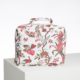 L'ABAT-JOUR SUR COMMANDE est une trousse à cosmétiques carrée de couleur blanche, ornée d'un motif floral et d'oiseaux colorés en rose, rouge et vert. Il est doté d'une fermeture à glissière et d'une petite poignée supérieure. Il est présenté sur une surface blanche sur un fond uni. la marque Toile de Jouy