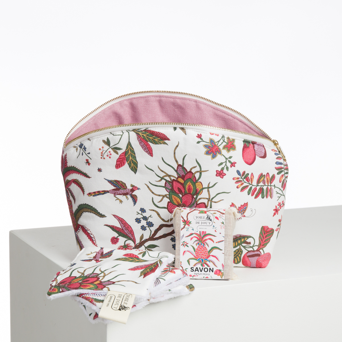 L'ABAT-JOUR SUR COMMANDE, un sac cosmétique blanc avec un intérieur rose et un motif floral coloré, est présenté sur une surface blanche avec des lingettes en tissu assorties et un savon en boîte. la marque Toile de Jouy