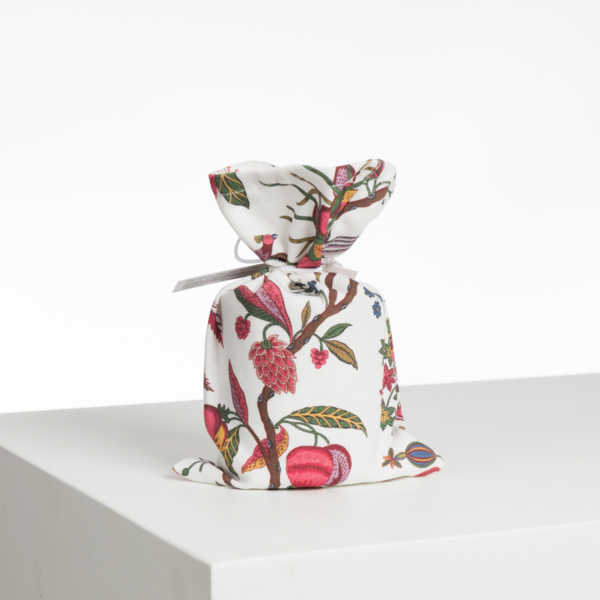 L'ABAT-JOUR SUR COMMANDE est une petite pochette en tissu présentant un motif floral et fruitier vibrant. Noué sur le dessus pour un effet froncé, il repose sur une surface blanche unie avec une simple toile de fond blanche. la marque Toile de Jouy