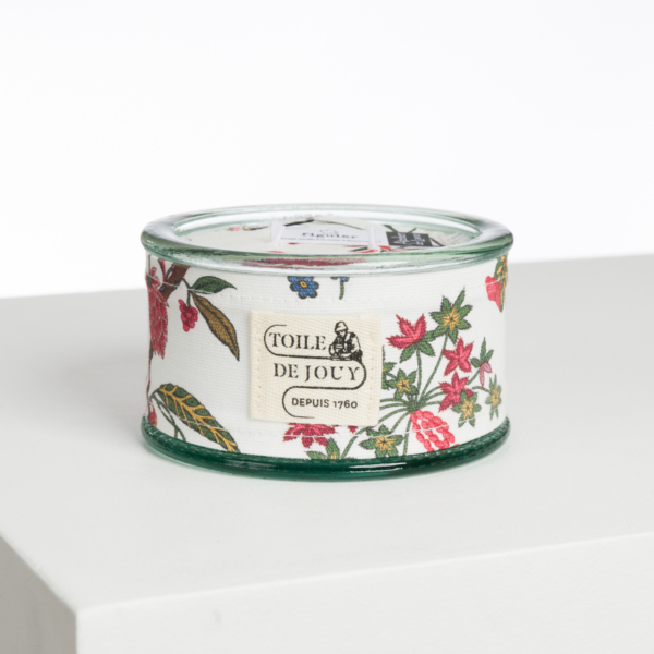 L'ABAT-JOUR SUR COMMANDE est un récipient rond en verre enveloppé d'un tissu blanc présentant un motif floral coloré et étiqueté "Toile de Jouy Depuis 1760", présenté sur une surface blanche sur un fond uni. la marque Toile de Jouy