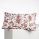ABAT-JOUR SUR COMMANDE est un coussin rectangulaire à fond blanc, décoré de motifs floraux et fruitiers roses, verts et rouges, avec un liseré rose foncé sur les bords. Il est présenté reposant sur une surface blanche. la marque Toile de Jouy