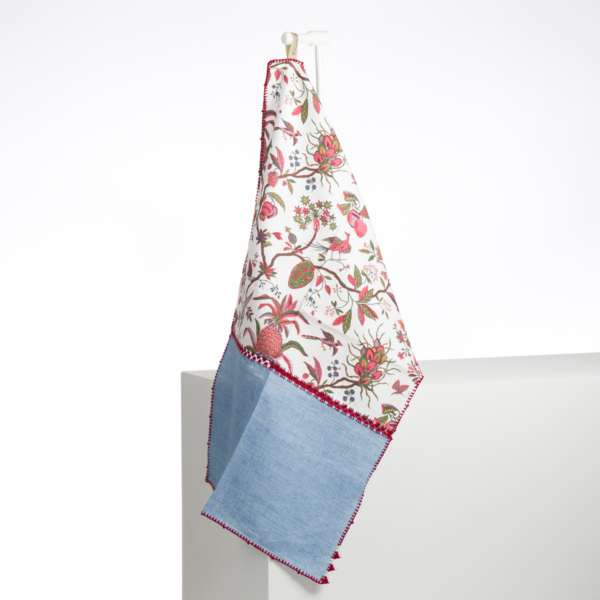 L'ABAT-JOUR SUR COMMANDE présente un motif floral et fruitier dans sa partie supérieure, une bordure rouge et une partie inférieure texturée bleu clair. Il est suspendu à un crochet blanc sur un fond blanc uni. la marque Toile de Jouy