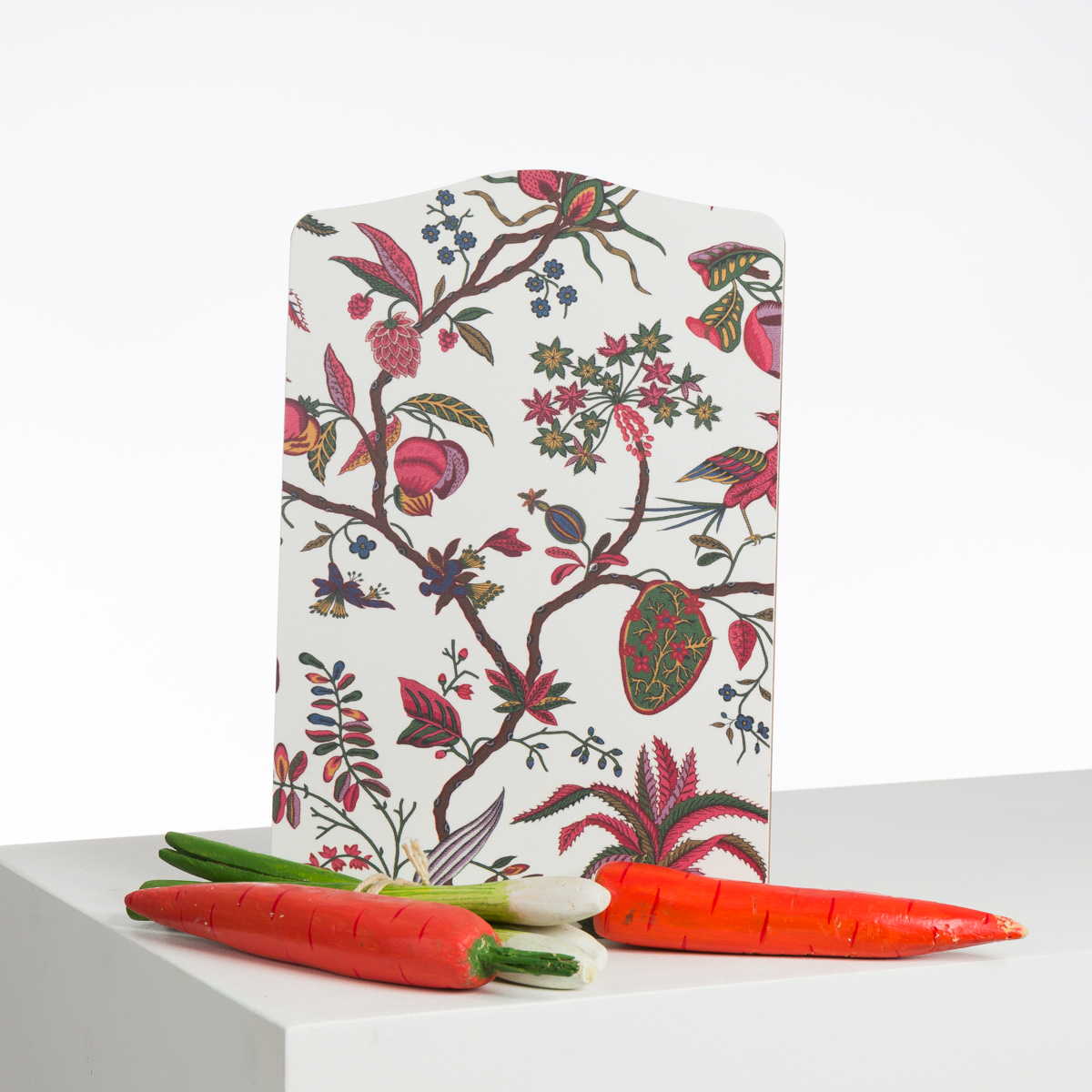 L'ABAT-JOUR SUR COMMANDE présente un motif floral et aviaire vibrant, présenté à la verticale sur une surface blanche, derrière trois répliques réalistes de carottes et d'oignons de printemps. la marque Toile de Jouy