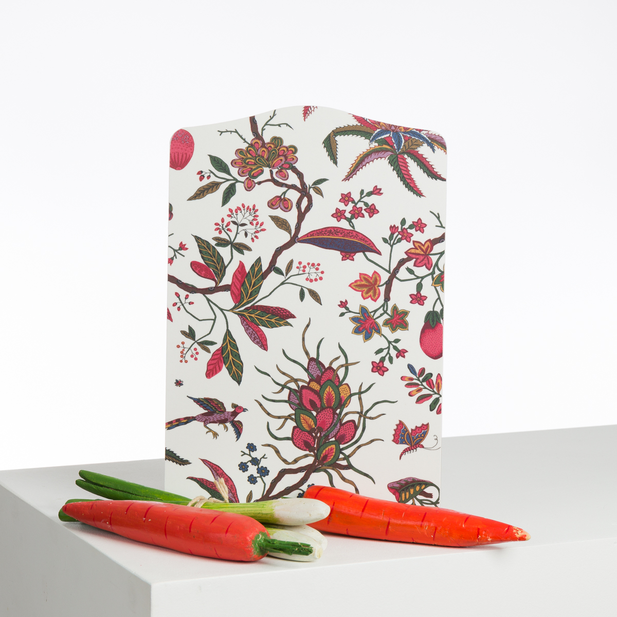 Un ABAT-JOUR SUR COMMANDE avec un paravent à motifs floraux se tient debout sur une surface blanche, avec deux carottes artificielles réalistes et trois oignons verts disposés en diagonale devant. la marque Toile de Jouy