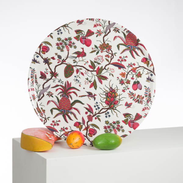 L'assiette ronde ABAT-JOUR SUR COMMANDE, au motif floral et fruitier joyeux, se tient debout sur une surface blanche, accompagnée de trois fruits en bois peints plus vrais que nature et d'un morceau de fromage réaliste. la marque Toile de Jouy