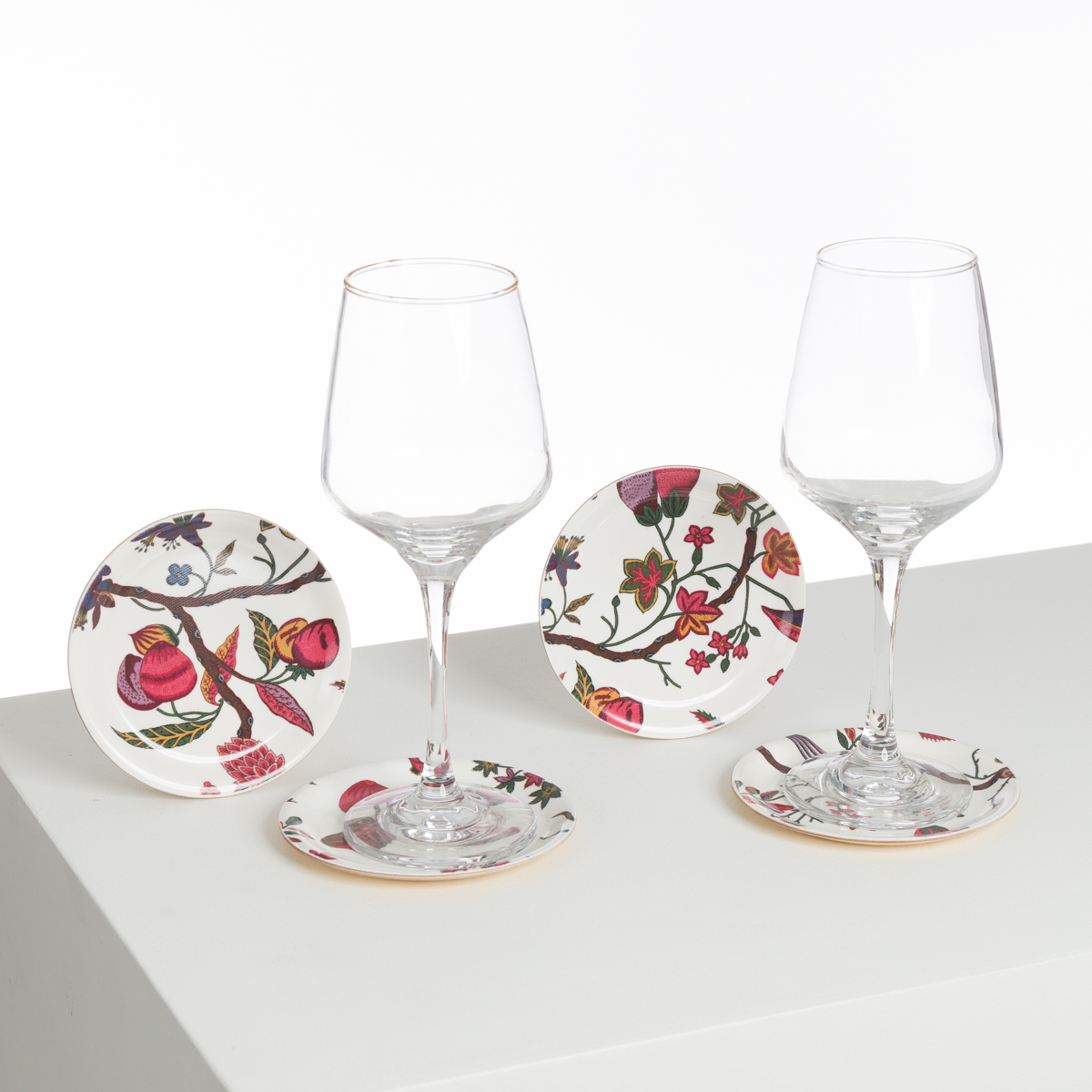 Trois verres à vin ABAT-JOUR SUR COMMANDE reposent chacun sur une petite assiette ronde ornée de motifs floraux et fruitiers colorés, posés sur une surface blanche sur un fond blanc uni. la marque Toile de Jouy