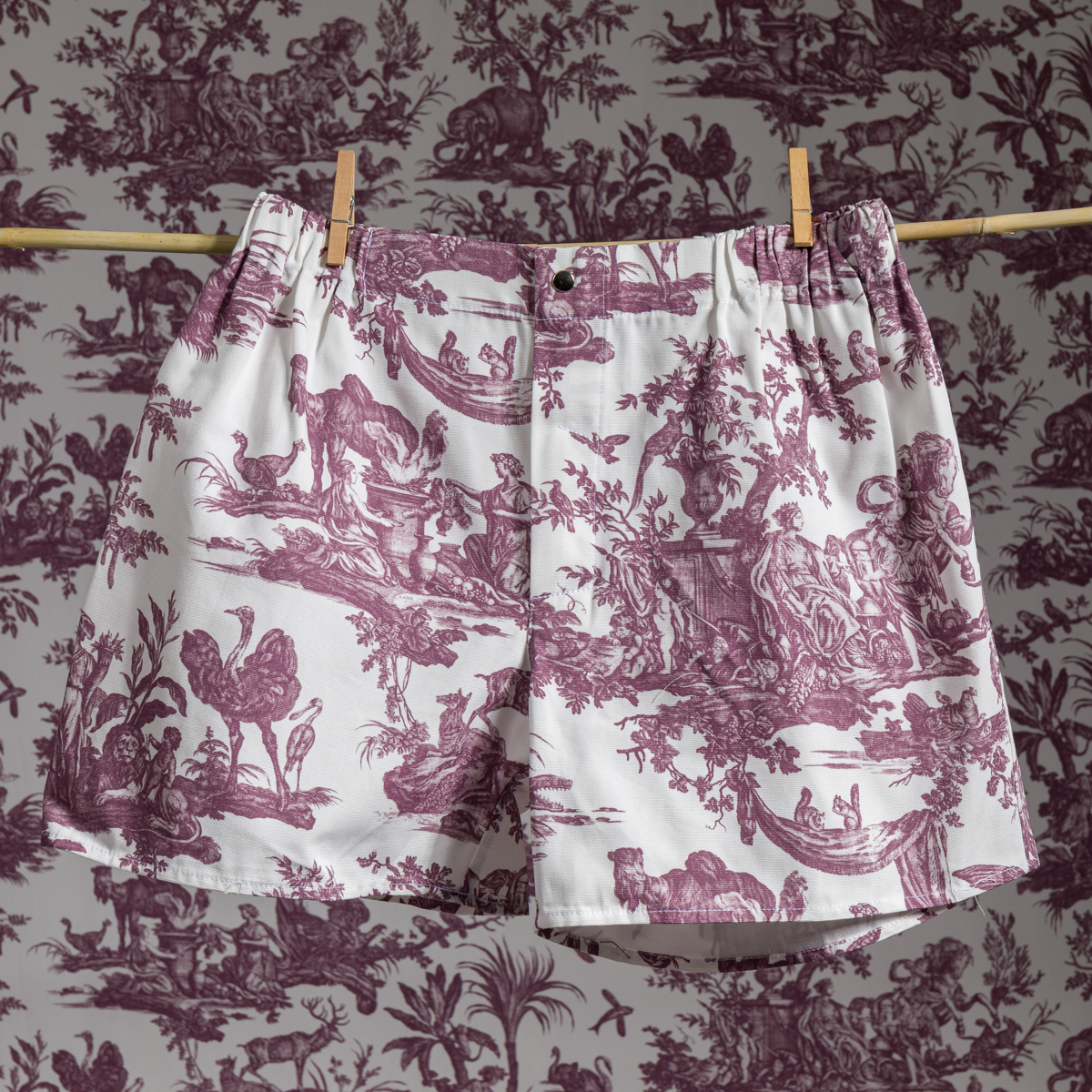 XCOMM_MICROFIBRE Le boxer ANANAS, avec son imprimé toile marron détaillé, est suspendu à une corde à linge avec des pinces à linge. Le papier peint qui se trouve derrière est assorti au motif complexe, ce qui permet au short de se fondre dans l'arrière-plan. la marque Toile de Jouy