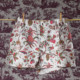 Un boxer blanc XCOMM_MICROFIBRE ANANAS avec un imprimé floral et de fruits tropicaux est suspendu à une corde à linge contre un mur à motifs de toile vintage. la marque Toile de Jouy
