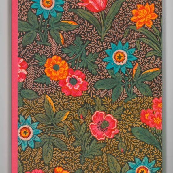 Le XCOMM_CARNET A5 BLEUETS est un carnet dont la couverture florale vibrante présente des fleurs rouges, orange, bleues et roses avec des feuilles vertes sur un fond sombre. Le dos est rose uni. la marque Toile de Jouy