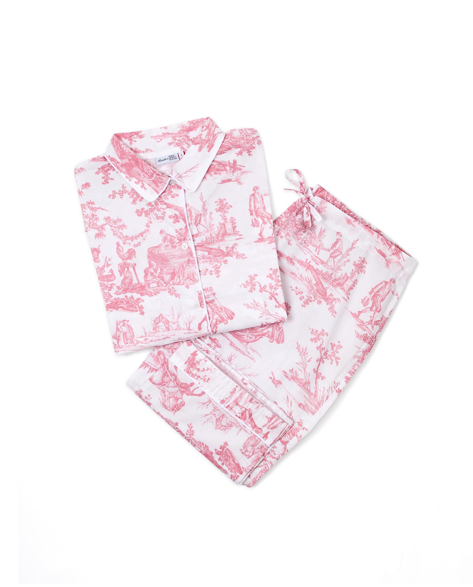 Le PYJAMA COURT FEMME "LES DELICES DES 4 SAISONS" ROSE-ACANTHE présente un pyjama blanc imprimé d'une toile rose, comprenant une chemise boutonnée à manches longues et un pantalon à cordon de serrage assorti, tous deux soigneusement pliés sur un fond blanc. la marque Toile de Jouy