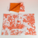 Le XCOMM_SET DE TABLE /2 FLEURS STYLISEES MANDARINE présente une serviette de table en tissu blanc avec un motif floral orange, étalée sur une surface, et une serviette pliée assortie au-dessus, montrant son verso en mandarine unie. la marque Toile de Jouy