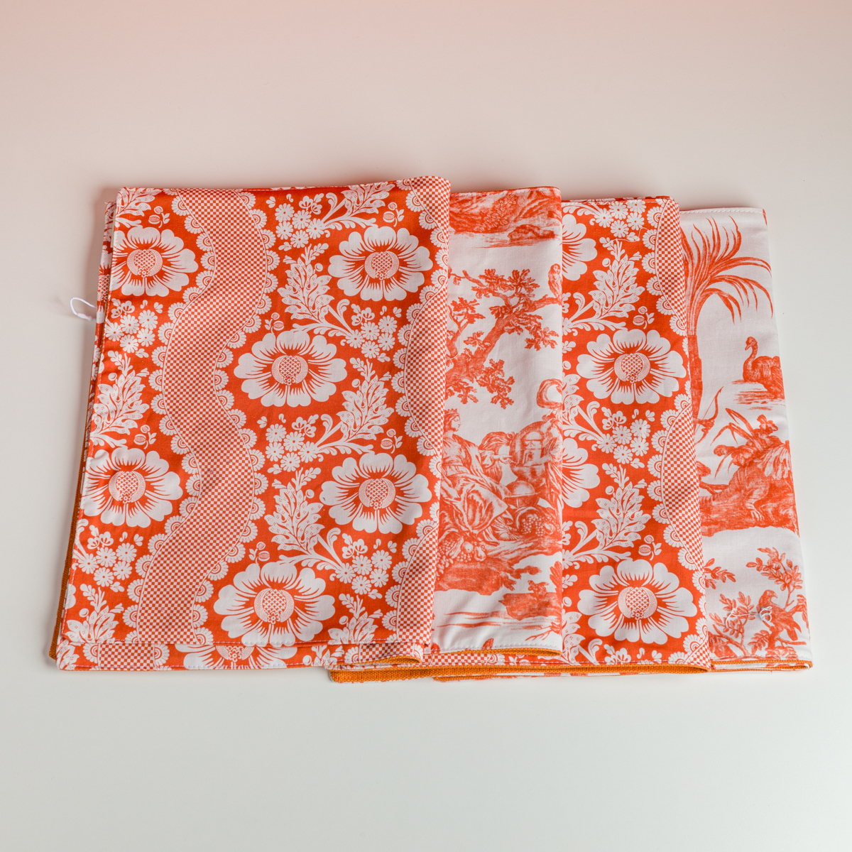Deux sets de table XCOMM_SET DE TABLE FLEURS STYLISEES MANDARINE, ornés de motifs floraux orange et blancs complexes, sont soigneusement disposés sur une surface claire. la marque Toile de Jouy
