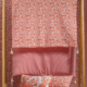 Une étagère en bois présente le tapis XCOMM_MATELAS DE REPOS FLEURS STYLISEES MANDARINE 190X90, un tapis à motifs roses et rouges avec une décoration florale ondulée, ainsi que des textiles coordonnés et un papier peint floral assorti à l'arrière-plan. la marque Toile de Jouy