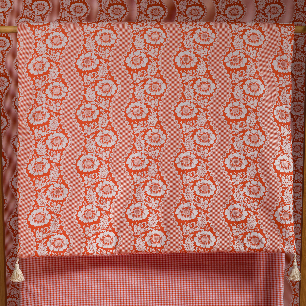 Le XCOMM_MATELAS DE REPOS FLEURS STYLISEES MANDARINE 190X90, qui présente des motifs floraux roses et rouges avec des rayures verticales ondulées, est présenté drapé sur une tringle contre un papier peint à motifs assortis pour un effet visuel superposé. la marque Toile de Jouy