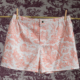 Le short CALEçON « FLEURS STYLISÉES » SAUGE, sur fond blanc orné d’un imprimé « toile » champêtre rose, est suspendu à des pinces à linge fixées sur une tringle en bois. L’arrière-plan présente un motif « toile » violet foncé assorti. la marque Toile de Jouy