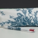 Le XCOMM_BIC ESCARPOLETTE BLEU, un stylo blanc orné d'un motif bleu, repose sur une surface blanche devant son étui assorti, décoré d'une illustration bleue représentant une personne assise tendant la main vers un oiseau. la marque Toile de Jouy