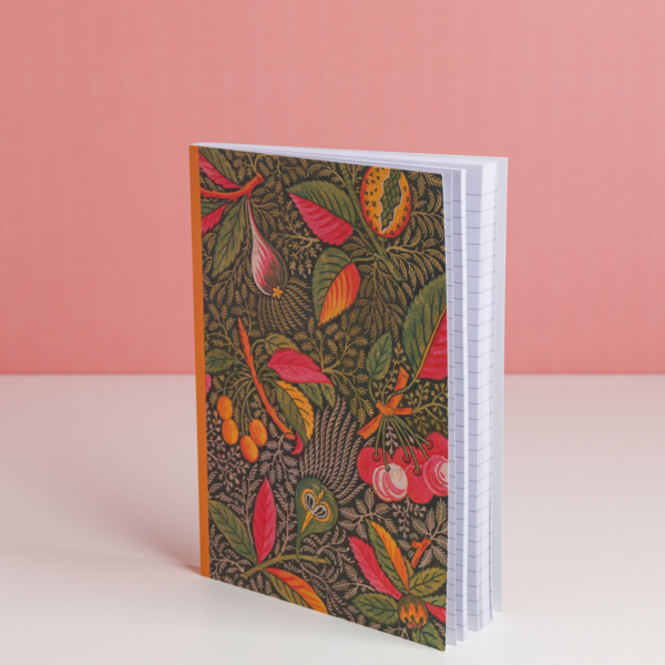 Le carnet EMPREINTE SOUS PASSE-PARTOUT "BONNES HERBES - BLEUETS" présente une couverture botanique vibrante avec des feuilles et des fruits, représentés debout sur une surface blanche sur un fond rose. A l'intérieur, les pages sont lignées. la marque Toile de Jouy