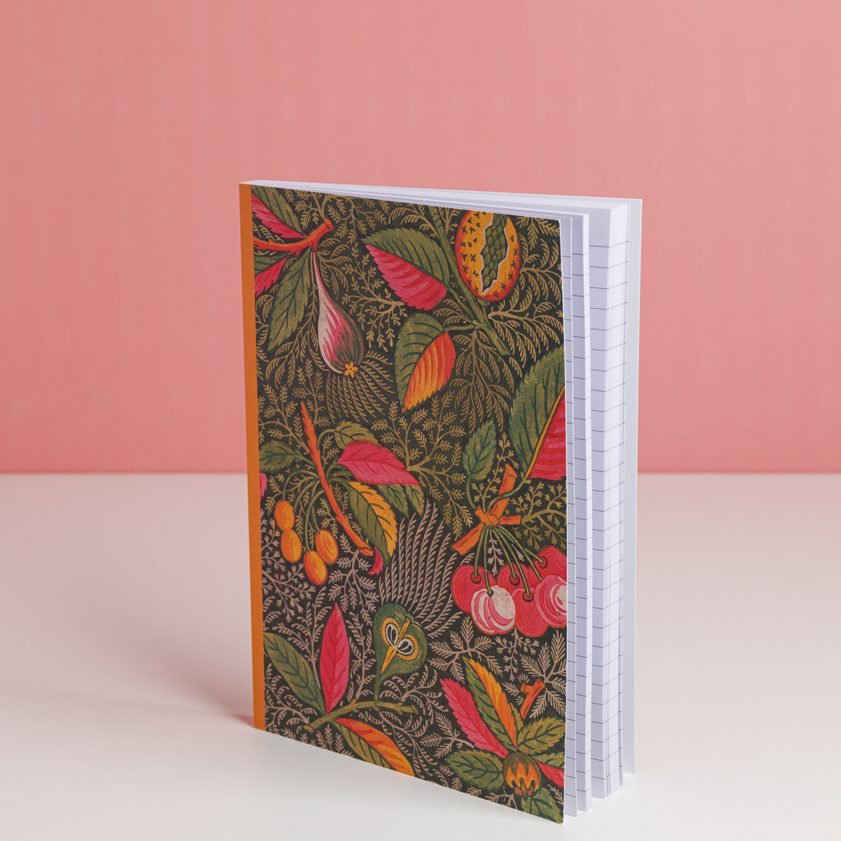 Le carnet EMPREINTE SOUS PASSE-PARTOUT "BONNES HERBES - BLEUETS" présente une couverture botanique vibrante avec des feuilles et des fruits, représentés debout sur une surface blanche sur un fond rose. A l'intérieur, les pages sont lignées. la marque Toile de Jouy