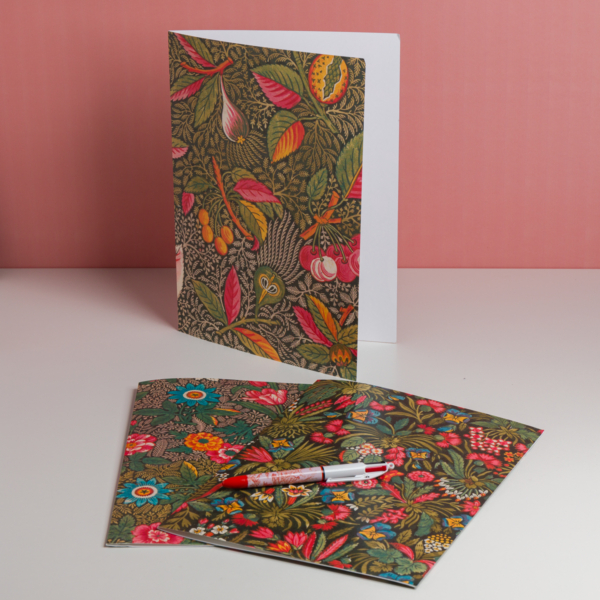 Trois cartes de vœux EMPREINTE SOUS PASSE-PARTOUT "BONNES HERBES - BLEUETS" aux motifs floraux éclatants sont présentées sur une surface blanche à fond rose - deux sont posées à plat sous un stylo, tandis qu'une se tient debout et partiellement ouverte. la marque Toile de Jouy
