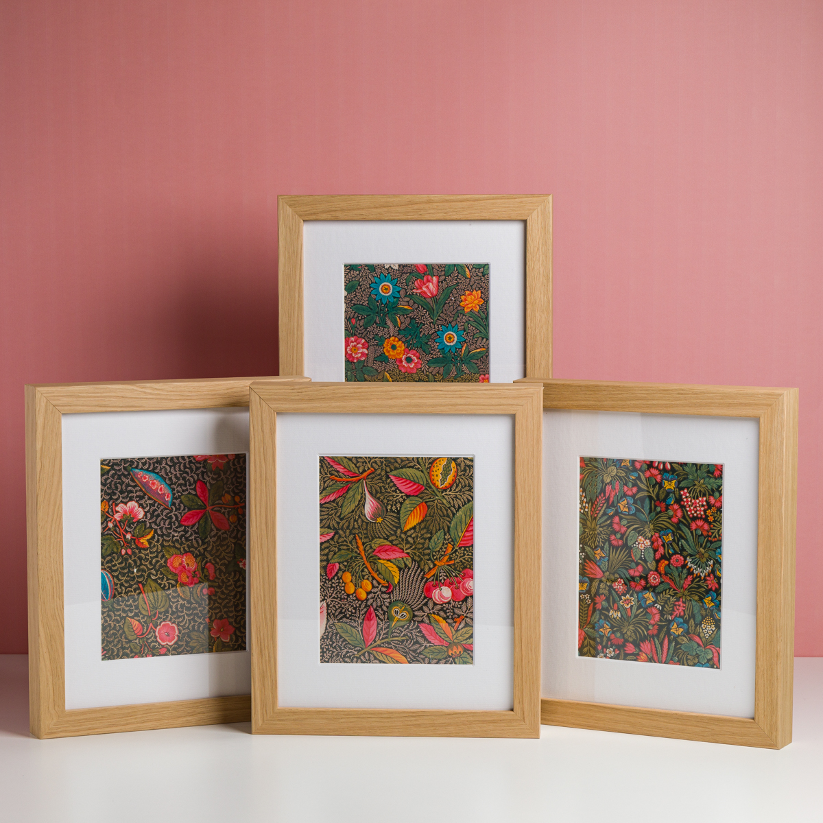 Quatre cadres en bois EMPREINTE SOUS PASSE-PARTOUT "BONNES HERBES - BLEUETS", aux motifs botaniques colorés et détaillés, sont présentés sur une surface blanche à fond rose. la marque Toile de Jouy