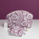 La pochette XCOMM_TROUSSE ARRONDIE FLEURS AMARANTE, une pochette à fermeture éclair à motif floral violet et blanc, accompagnée de disques démaquillants réutilisables assortis et d’une étiquette de marque, est présentée sur une surface blanche devant un fond violet. la marque Toile de Jouy