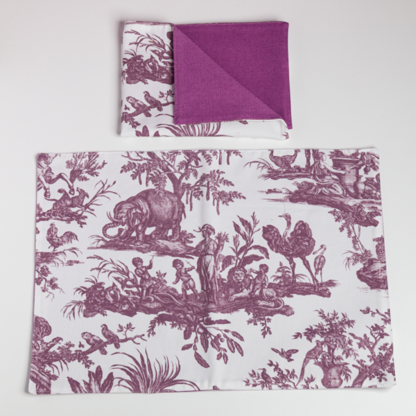 Le XCOMM_SET DE TABLE /2 FLEURS STYLISEES SAUGE comprend un set de table blanc et une serviette pliée avec des motifs floraux stylisés en sauge ; la serviette présente également un côté en sauge unie. Les deux sont disposés sur un fond blanc. la marque Toile de Jouy