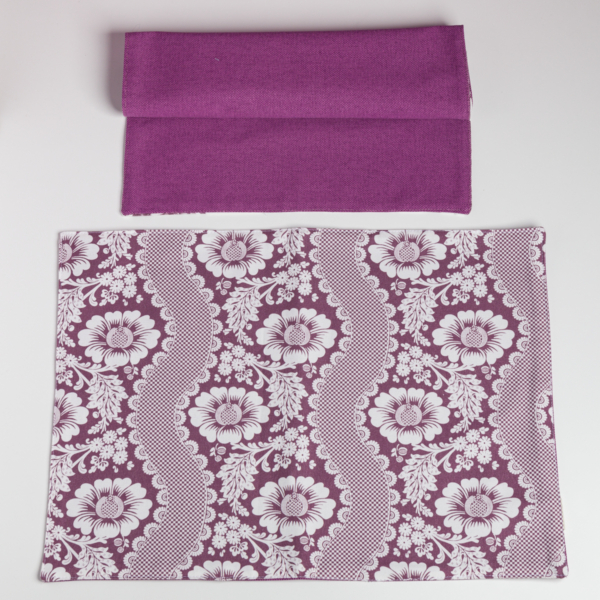 Un XCOMM_SET DE TABLE /2 FLEURS STYLISEES SAUGE plié se trouve au-dessus d'une pièce rectangulaire avec un motif floral blanc et de la dentelle, tous deux présentés sur un fond blanc. la marque Toile de Jouy