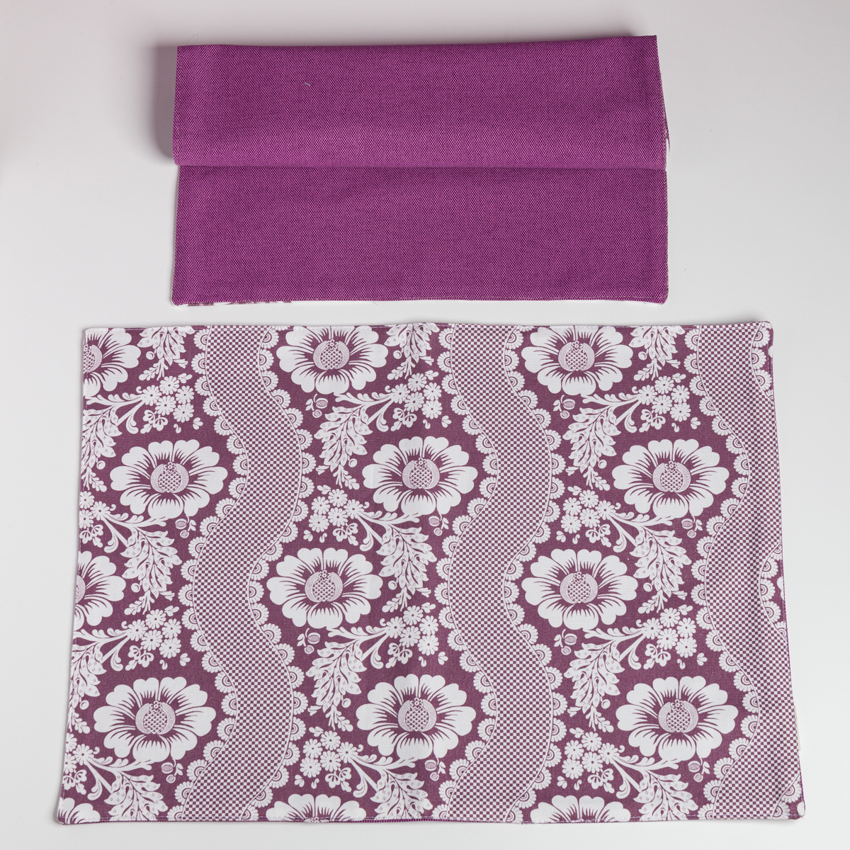 Un XCOMM_SET DE TABLE /2 FLEURS STYLISEES SAUGE plié se trouve au-dessus d'une pièce rectangulaire avec un motif floral blanc et de la dentelle, tous deux présentés sur un fond blanc. la marque Toile de Jouy