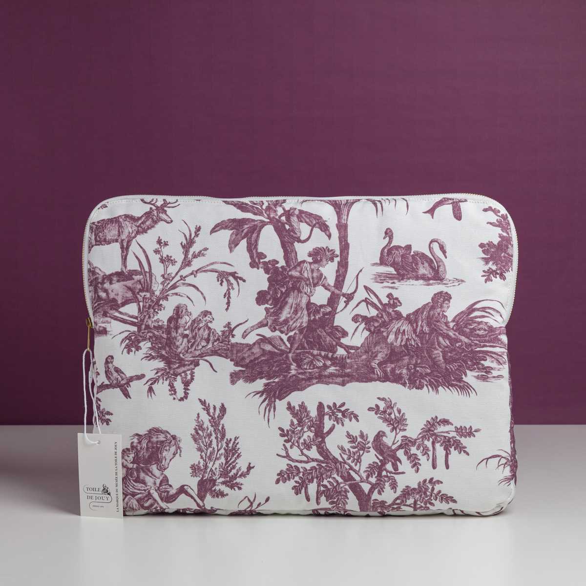 La XCOMM_HOUSSE ORDI 4 APRTIES AMARANTE est une housse pour ordinateur portable avec un motif de toile pastorale violette représentant des animaux et des personnes sur un fond assorti, avec une petite étiquette blanche sur la fermeture à glissière gauche. la marque Toile de Jouy